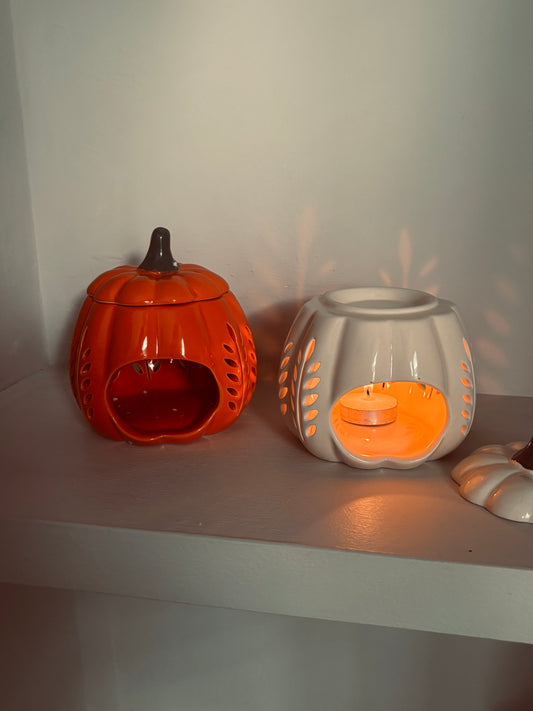 Two ceramic pumpkin-shaped lanterns on a white surface with a plain background.