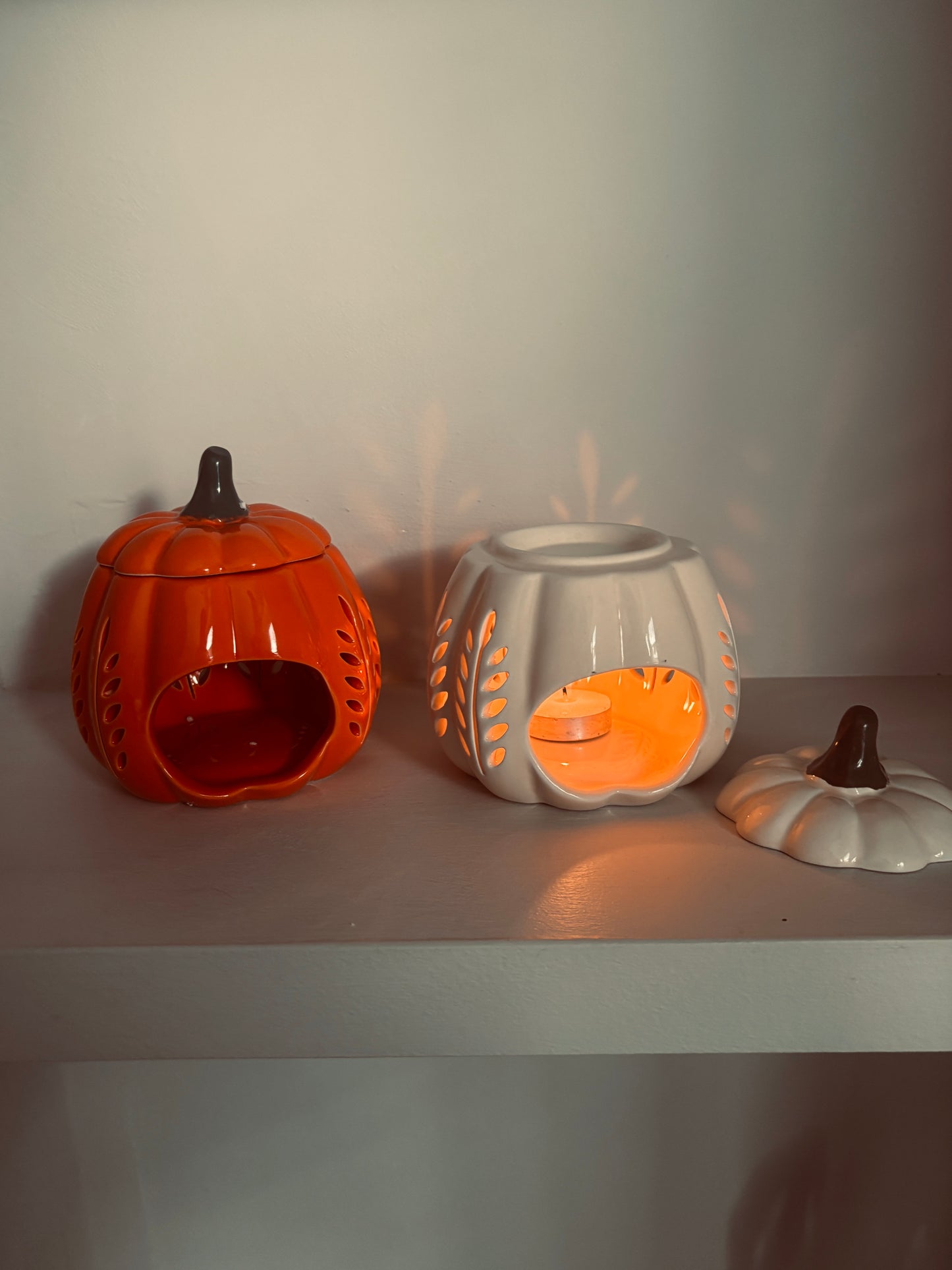 Two ceramic pumpkin-shaped containers on a white surface with a plain background