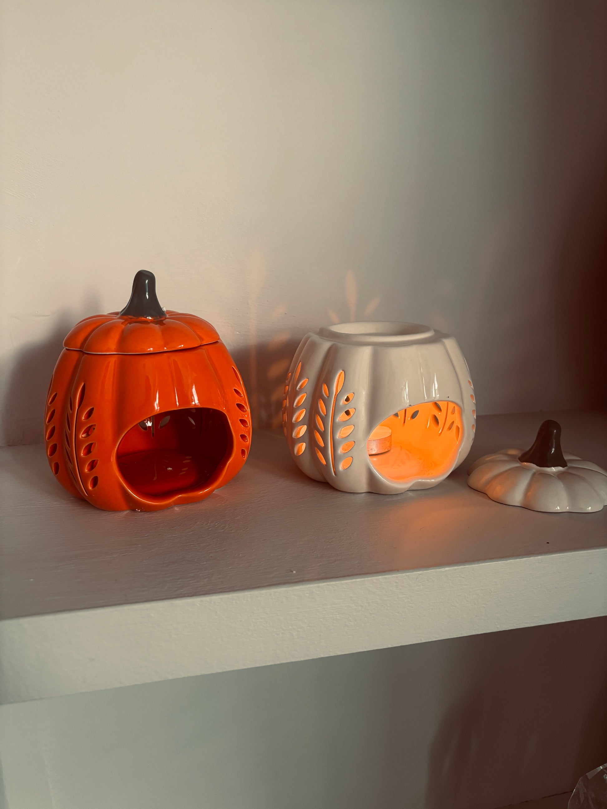 Three ceramic pumpkin-shaped lanterns on a shelf with a neutral background