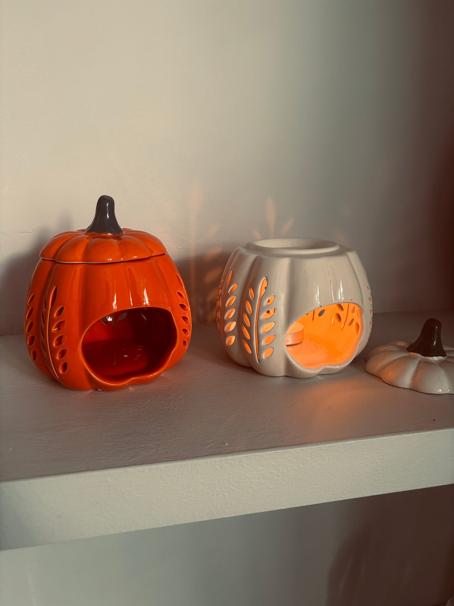 Two ceramic pumpkin-shaped lanterns on a shelf with a neutral background
